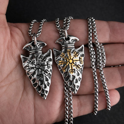 Two silver arrowhead pendants on chains held in a hand against a dark background